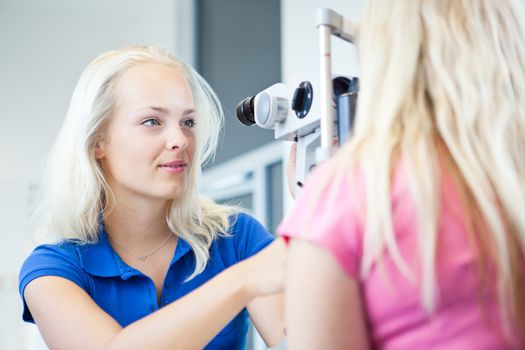 optometry concept - pretty, young female patient having her eyes examined by an eye doctor (color toned image; shallow DOF)