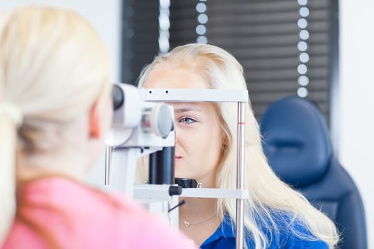 optometry concept - pretty, young female patient having her eyes examined by an eye doctor (color toned image; shallow DOF)