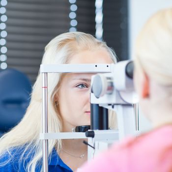 optometry concept - pretty, young female patient having her eyes examined by an eye doctor (color toned image; shallow DOF)