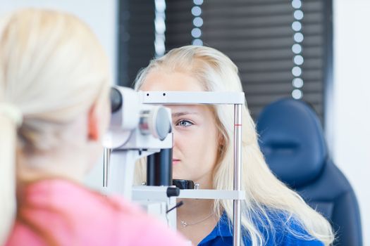 optometry concept - pretty, young female patient having her eyes examined by an eye doctor (color toned image; shallow DOF)