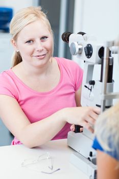 optometry concept - pretty, young female patient having her eyes examined by an eye doctor (color toned image; shallow DOF)