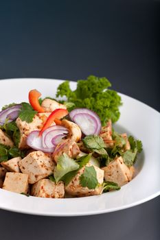 A freshly prepared Thai food stir fry dish with tofu red onions and peppers presented on a round white dish.