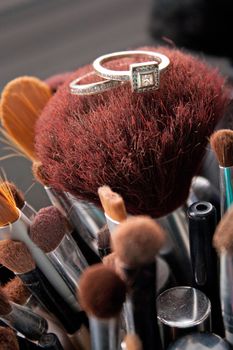 Two diamond rings resting upon some makeup brushes.  One is a diamond engagement ring and the other is a wedding band. Shallow depth of field.