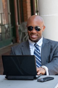 A handsome African American business man in his early 30s working on his laptop or netbook computer with his cell phone nearby.