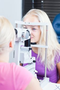 optometry concept - pretty, young female patient having her eyes examined by an eye doctor (color toned image; shallow DOF)