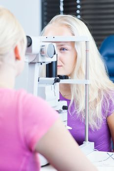 optometry concept - pretty, young female patient having her eyes examined by an eye doctor (color toned image; shallow DOF)