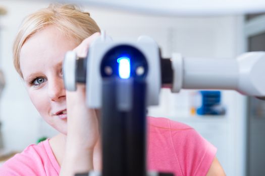 optometry concept - portrait of a young pretty optometrist using slit lamp (color toned image)