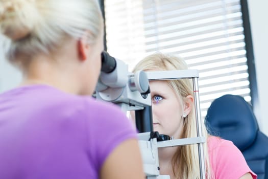 optometry concept - pretty, young female patient having her eyes examined by an eye doctor (color toned image; shallow DOF)