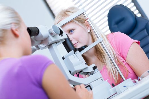 optometry concept - pretty, young female patient having her eyes examined by an eye doctor (color toned image; shallow DOF)