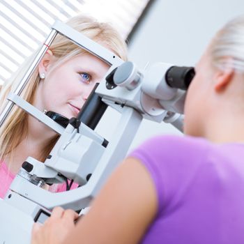 optometry concept - pretty, young female patient having her eyes examined by an eye doctor (color toned image; shallow DOF)