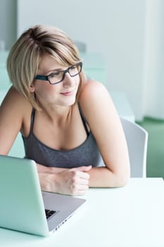 Portrait of a young woman pensively looking out of the window while sitting in front of her laptop