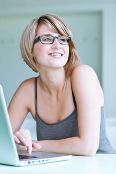 Portrait of a young woman pensively looking out of the window while sitting in front of her laptop