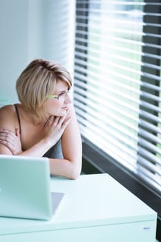 Portrait of a young woman pensively looking out of the window while sitting in front of her laptop