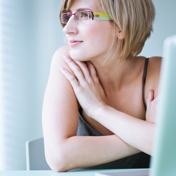 Portrait of a young woman pensively looking out of the window while sitting in front of her laptop