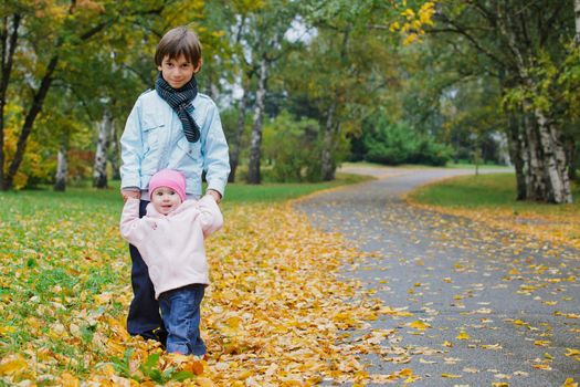 Older brother walking with his year old sister in the autumn park