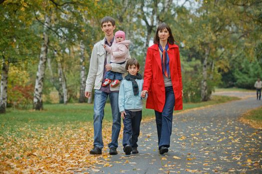 Happy family in park. Father, mother with daughter and son walking in the autumn park