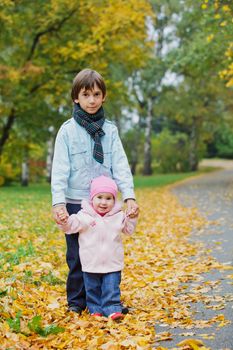Older brother walking with his year old sister in the autumn park. Vertical view
