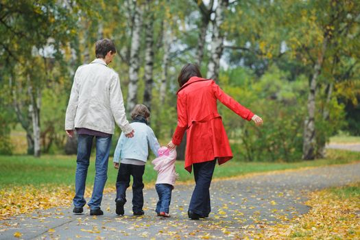 Happy family in park. Father, mother with daughter and son walking in the autumn park