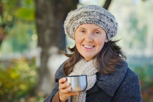 Young pretty woman drinks tea in autumn park