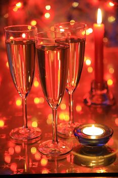 Champagne in glasses, candle and blured lights on red background