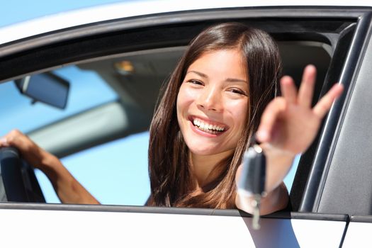 Woman driving showing car keys out the window. Young female driving happy about her new car or drivers license. Beautiful mixed race Caucasian / Asian driver.