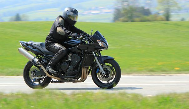 Biker wearing black clothes and driving a big motobike in the countryside