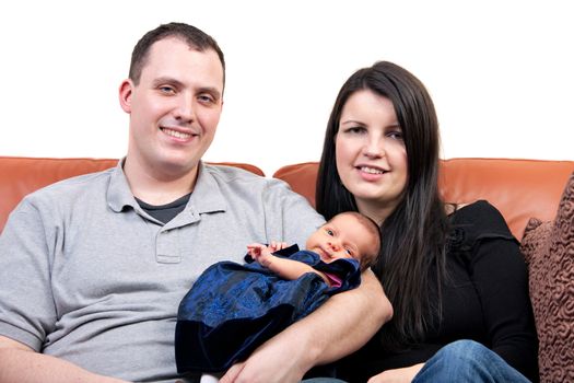 A young happy and healthy family seated on a couch holding their newborn daughter.