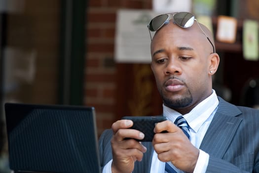 A good looking African American business man works on his laptop or netbook computer with a smart phone in his hands.