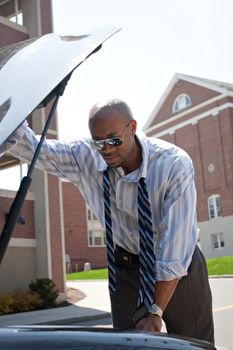 A business man having a bad day checks under the hood of his car to figure out what the problem is.