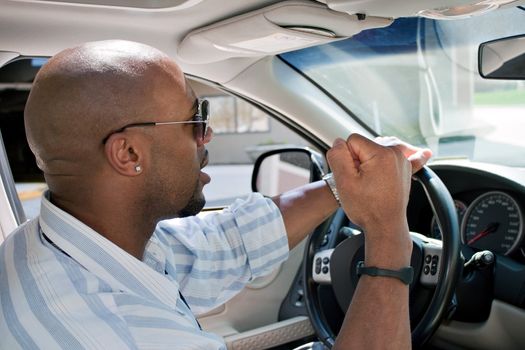 An irritated man driving a car is expressing his road rage with his fist clenched in the air.