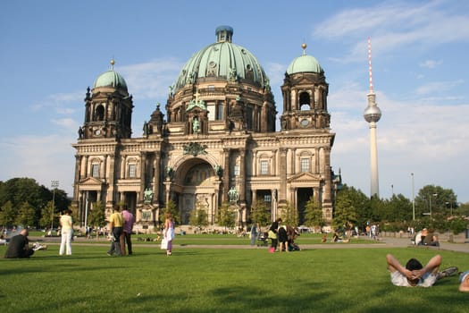 Tourists on the lawn in front of the Berlin Cathedral, with the TV tower behind it