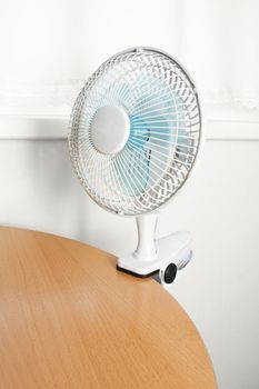 Small table fan is attached to the edge of the table.