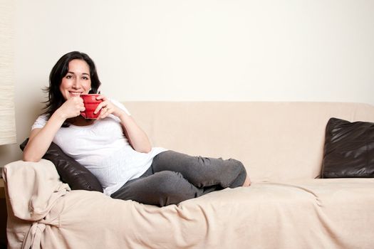 Beautiful happy young woman sitting relaxed laid back on sofa couch in livingroom drinking a beverage.