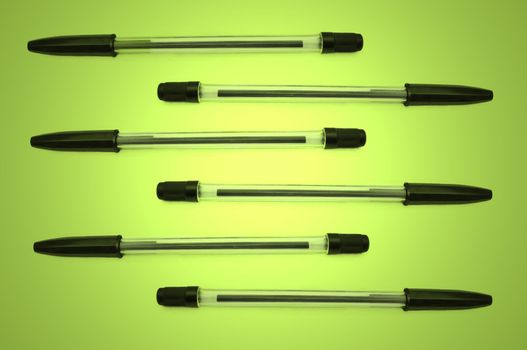 Six black biro pens arranged horizontally in formation over green and yellow light effect