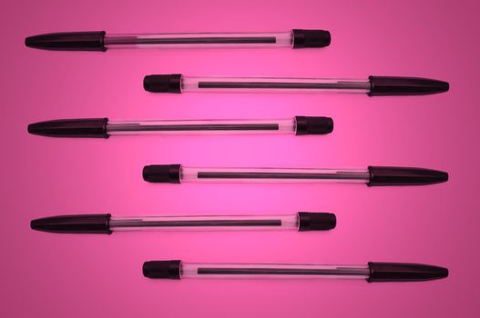 Six black biro pens arranged horizontally in formation over pink light effect