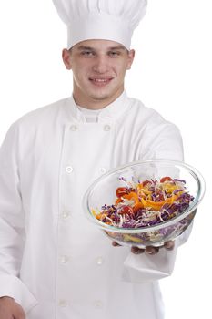 The young chef in uniform and chef's hat stretches salad in a bowl.