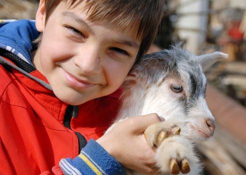 teenage boy portrait with young white goatling smiling outdoor