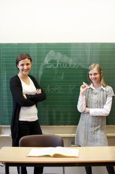 Teacher and pupil at the blackboard. The student has the words "School is great" written on the blackboard  