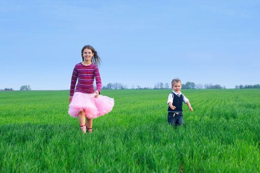 A beautiful sister runing with her cute little brather on the grass