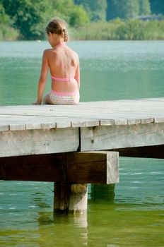Cute little girl sitting on a pier and looking at the water. Vertical view