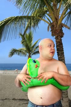 A large man with inflatable toy gets ready to go into the ocean.
