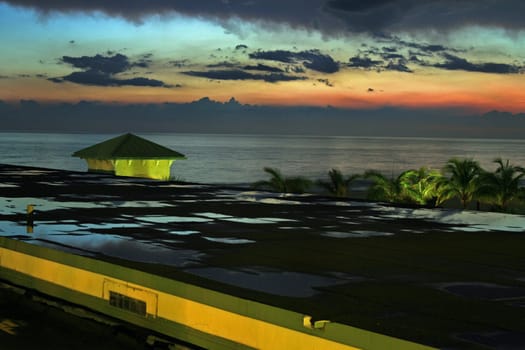 A sunset reflected in the puddles on a building, with view of the ocean.