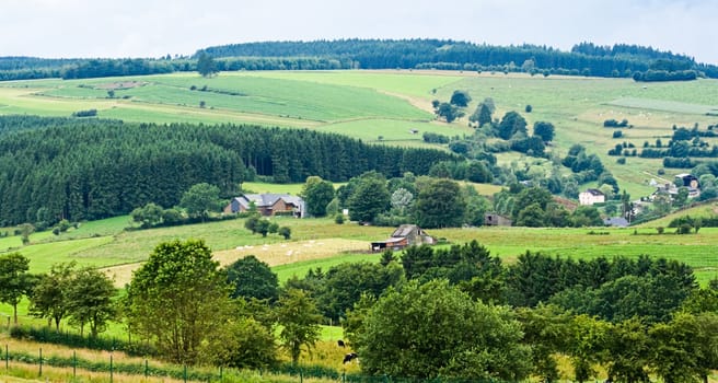 Agricultural landscape with meadows, hills and farms on cloudy summerday