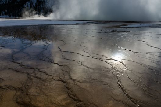 The sun and a forested ridge reflected in shallow water, Grand Prismatic Spring, Yellowstone National Park, Wyoming, USA