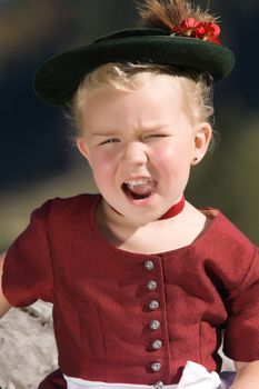 Little blonde girl in typical Bavarian costume and singing on the mountain