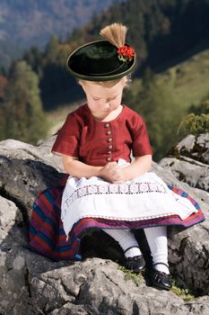 Little blonde girl in typical Bavarian costume on the mountain and pray