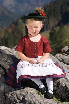 Little blonde girl in typical Bavarian costume on the mountain