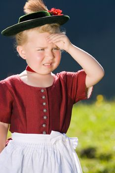 Little blonde girl in typical Bavarian costume on the mountain and looks into the country