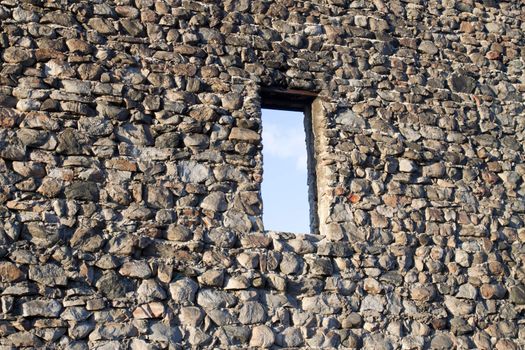 Wall of an old abandoned castle overlooking the blue sky through the window