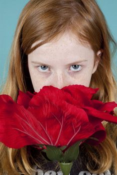 young girl is looking at you over a big red rose